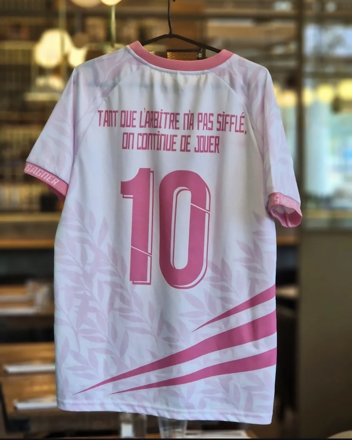 Un maillot solidaire MAIDESEIN blanc et rose suspendu dans la brasserie, vu de dos : « Tant que l’arbitre n’a pas sifflé, on continue de jouer » et le numéro 10