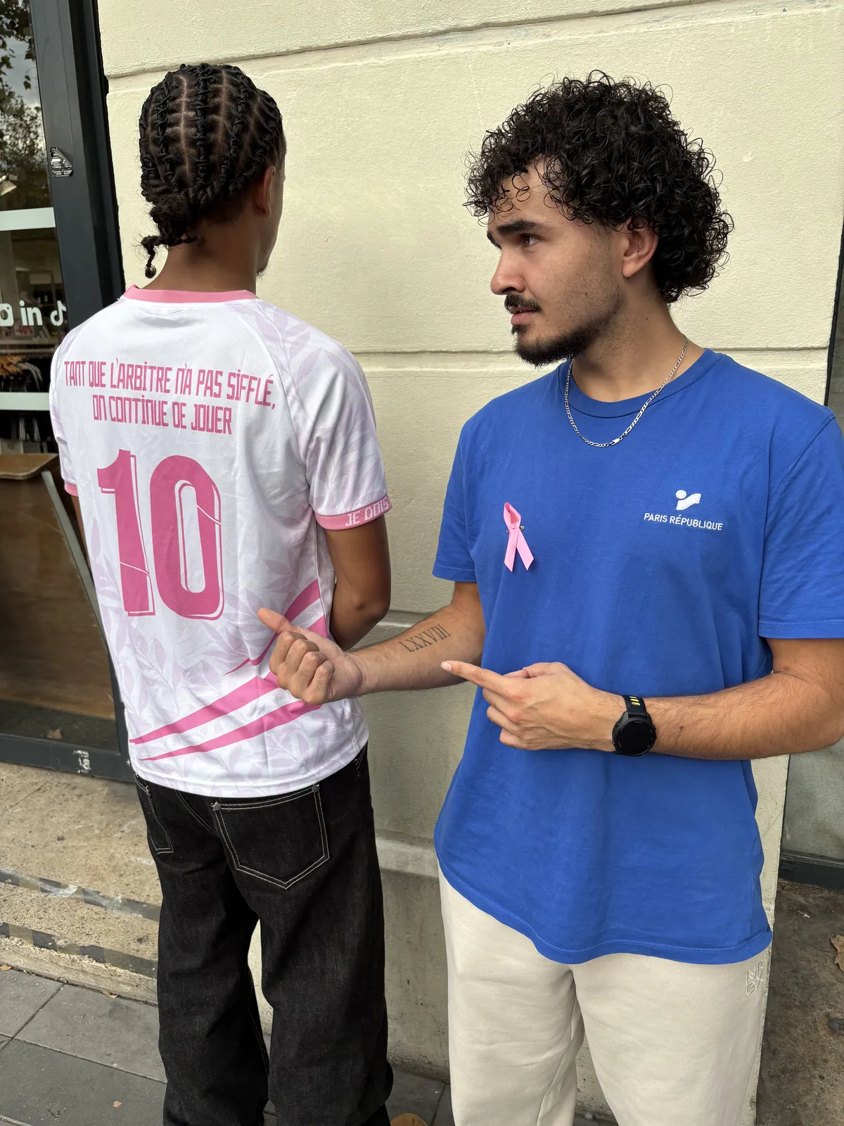Devant le magasin Intersport Paris République, un vendeur portant le ruban rose montre le dos d’un maillot solidaire MAIDESEIN porté par un jeune homme