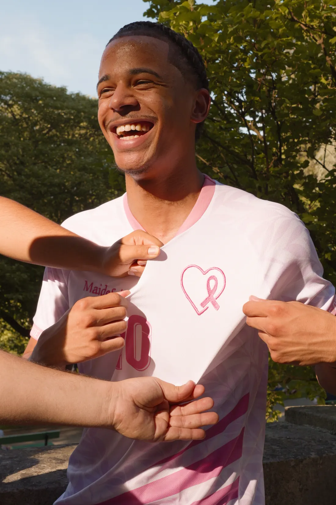 Un jeune homme éclate de rire pendant que des mains tendent son maillot MAIDESEIN pour montrer le logo en forme de cœur